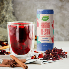 Elegant presentation of Taltis Foods Hibiscus Infusion carbonated drink, 355 mL can next to a glass filled with the beverage, surrounded by dried hibiscus flowers and spices.