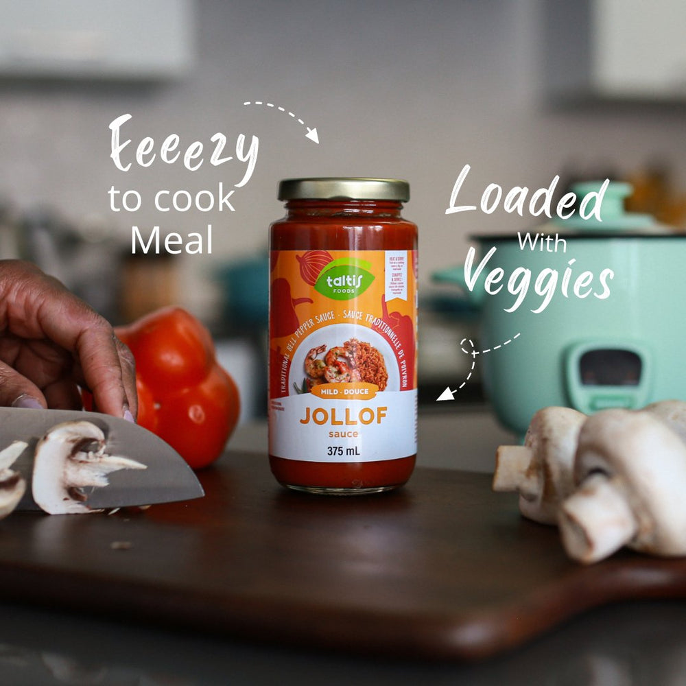 Homely kitchen scene with a jar of Taltis Foods Mild Jollof Sauce, 375 mL, on a countertop, with text overlay stating 'Eeezy to cook Meal' and 'Loaded With Veggies'. Fresh tomatoes and sliced mushrooms are being prepared in the background, emphasizing the sauce's ease of use and healthy attributes.